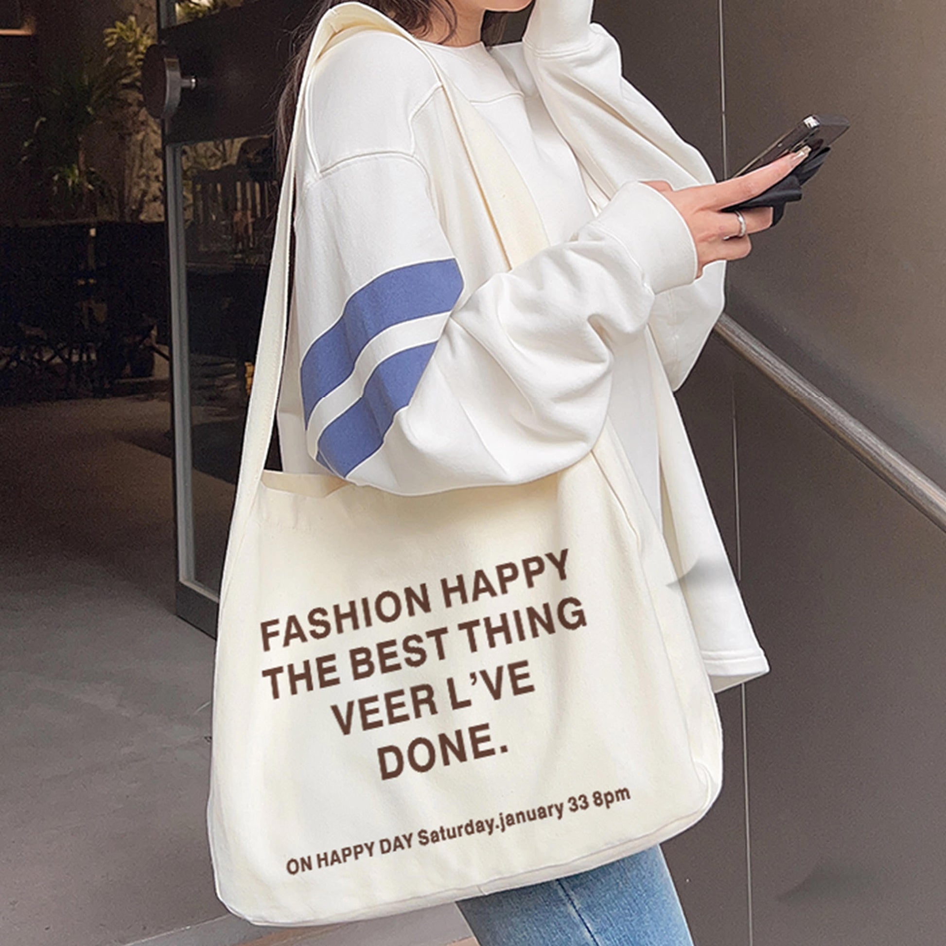 A woman in a blue jeans, and white sneakers holds a personalized tote bag with the words "Fashion Happy The Best Thing Veer L've Done" printed on it.     