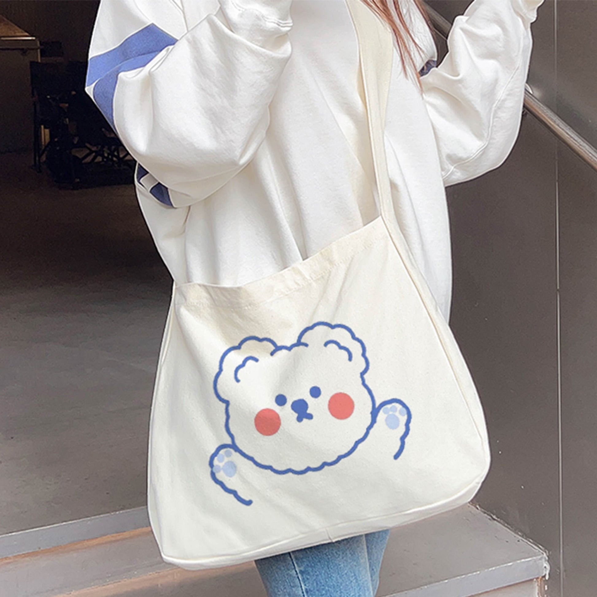 A person in blue jeans and white sneakers is wearing a personalized white crossbody bag with a teddy bear printed on it.