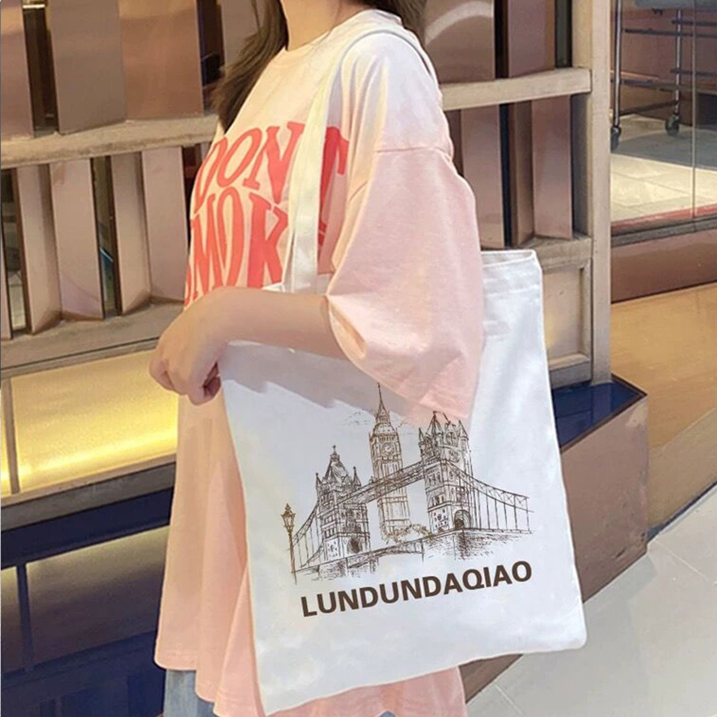 A girl wearing a pink t-shirt holds a white personalized tote bag featuring a printed illustration design.