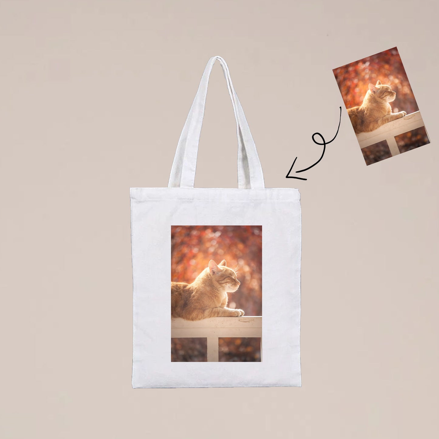 A photo of a custom photo tote bag. The tote bag is white and has a photo of a cat on it. The cat is a brown tabby cat. 