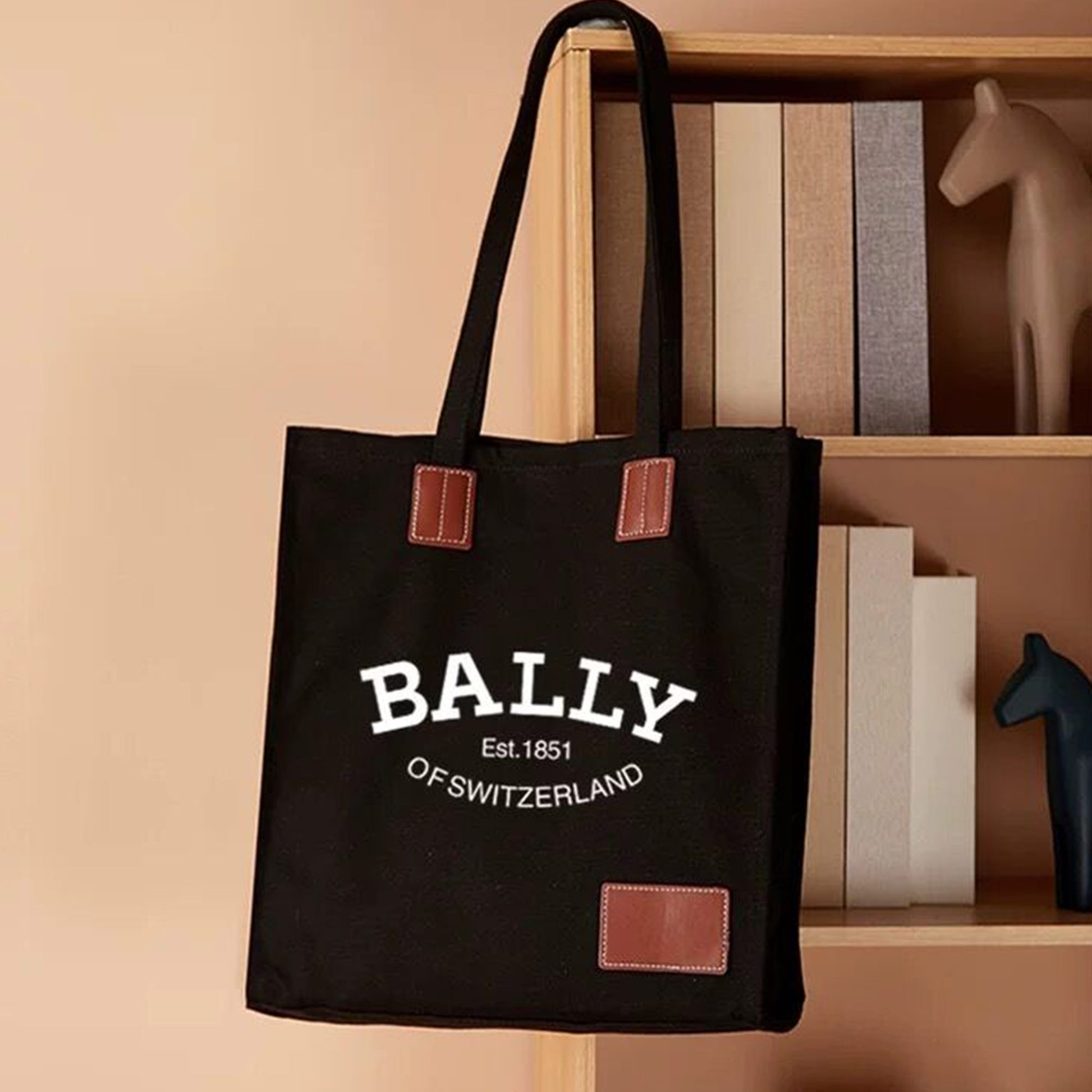 A black custom photo tote bag with an image of a dog on it hangs on the bookshelf. The tote bag is thick and in good shape.